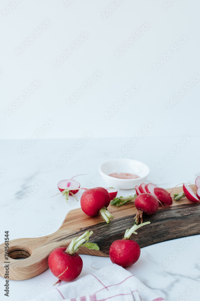 chopped radishes lie on a wooden cutting board, next to a kitchen towel and whole radishes on a marble background chopped radishes lie on a wooden cutting board, next to a kitchen towel and whole radishes on a marble background