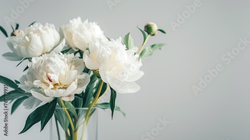 White peonies in a glass vase against a neutral background.
