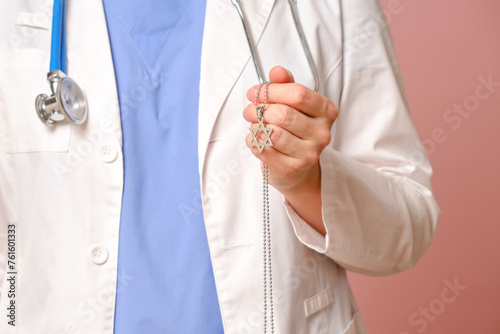 Woman doctor holding Jewish religious symbol, studio pink background. Nurse in uniform with stethoscope on red studio background © Андрей Журавлев