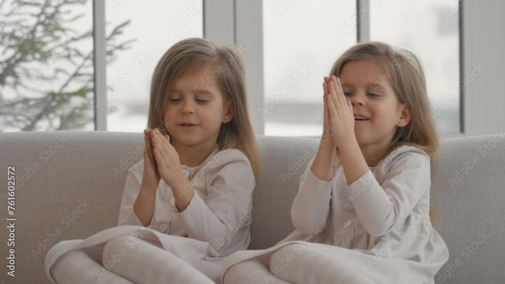 Two children twins playing at home. Happy cheerful mischievous little sisters twins sitting on sofa, smiling and laugh, playing in living room at home close up. Sisters' friendship love concept.