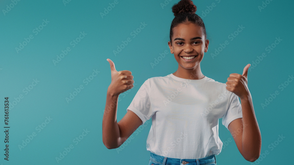 A cheerful young woman with a bun hairstyle smiles at the camera and gives a double thumbs-up against a blue background A cheerful young woman with a bun hairstyle smiles at the camera and gives a double thumbs-up against a blue background