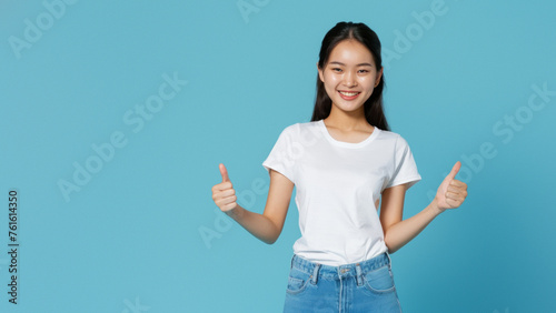 Pleasant Asian woman in casual attire gives a confident thumbs up gesture on a solid color background