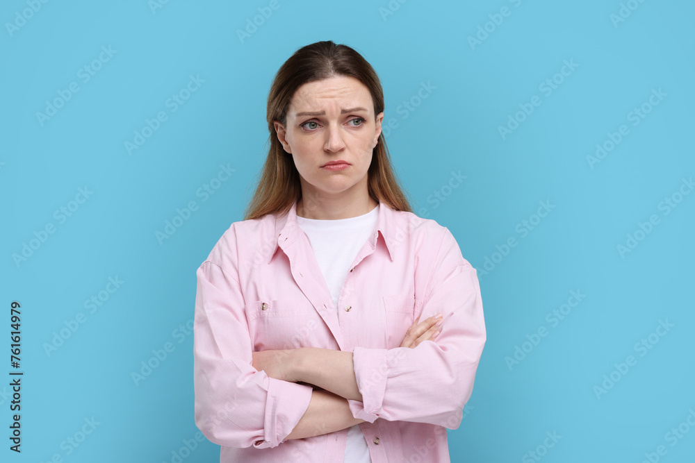 Portrait of sad woman with crossed arms on light blue background Portrait of sad woman with crossed arms on light blue background