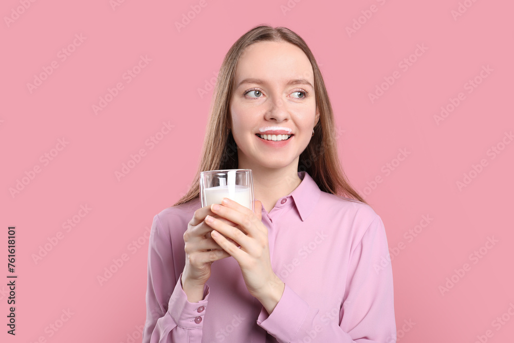 Smiling woman with milk mustache holding glass of tasty dairy drink on pink background Smiling woman with milk mustache holding glass of tasty dairy drink on pink background