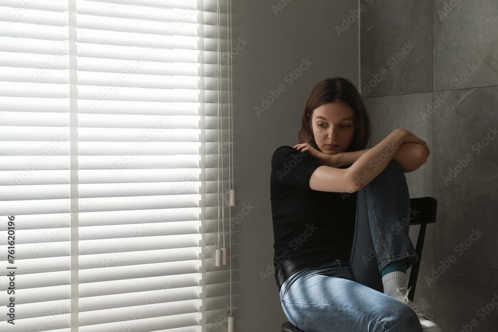 Fototapeta premium Sad young woman sitting on chair indoors, space for text