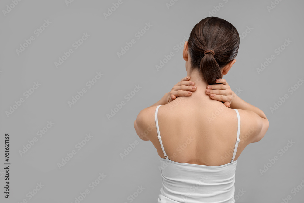 Woman touching her neck on grey background, back view. Space for text Woman touching her neck on grey background, back view. Space for text