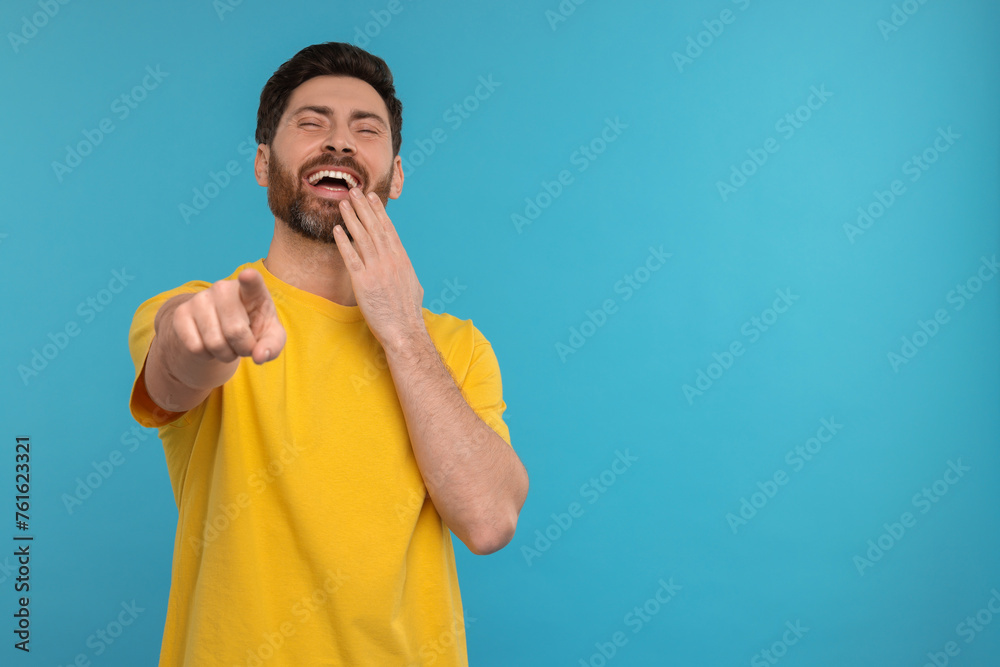 Handsome man pointing at something and laughing on light blue background. Space for text Handsome man pointing at something and laughing on light blue background. Space for text