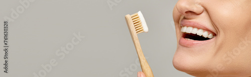 cropped view of joyful woman holding toothbrush with toothpaste and smiling on grey backdrop. banner