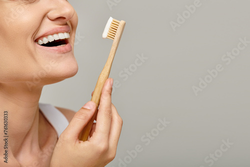cropped shot of joyful woman holding toothbrush with toothpaste and smiling on grey backdrop