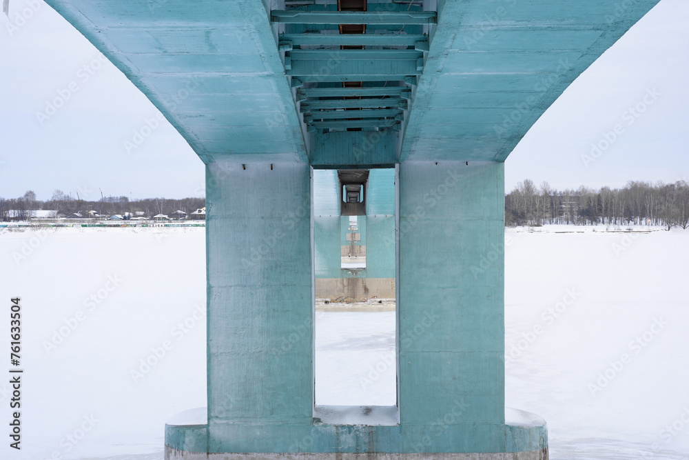 Close-up of part of the support of a metal road-railway bridge, over a river covered with white ice