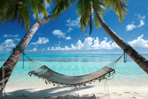 A hammock is hanging between two palm trees on a beach