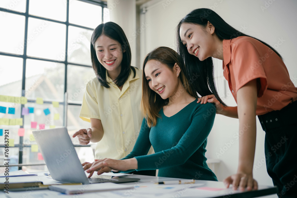 Fototapeta premium Three women are sitting at a table looking at a laptop