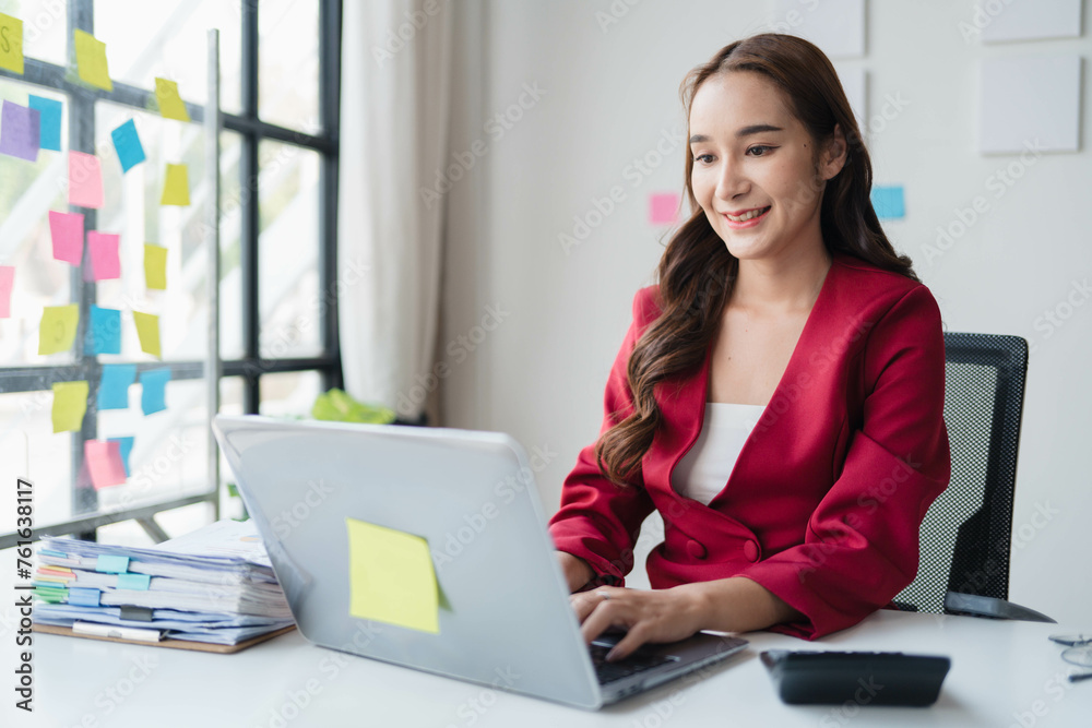 A woman in a red jacket is sitting at a desk with a laptop A woman in a red jacket is sitting at a desk with a laptop