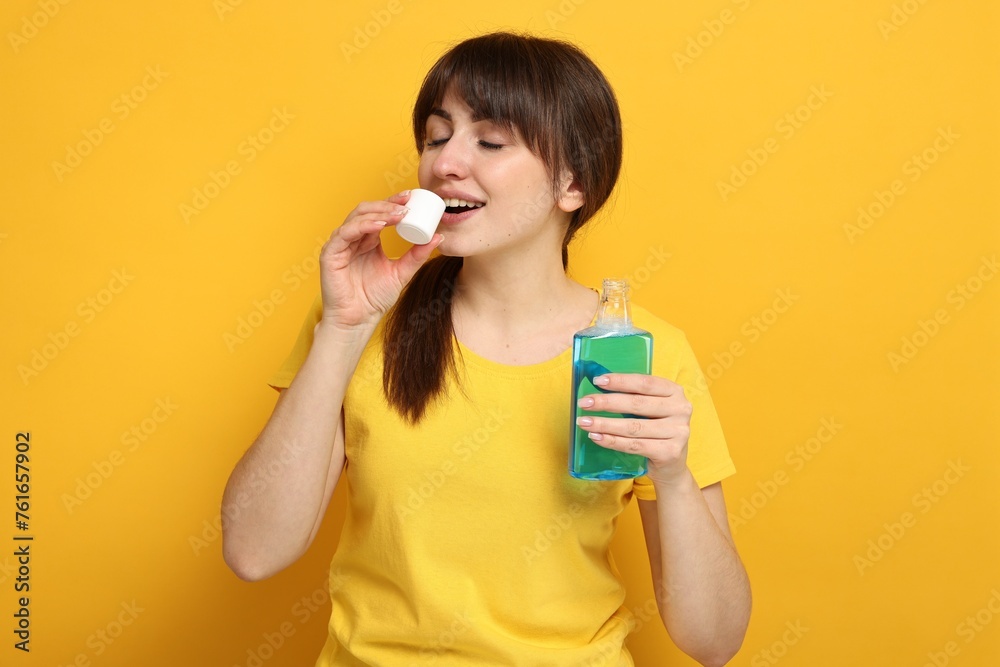 Young woman using mouthwash on yellow background Young woman using mouthwash on yellow background