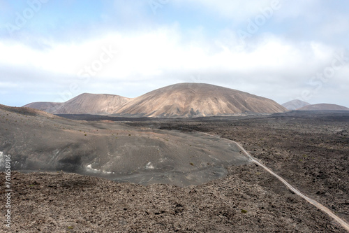 A road going through lava fields towards multiple small volcanoes in Timanfaya National park, Lanzarote, Canary islands