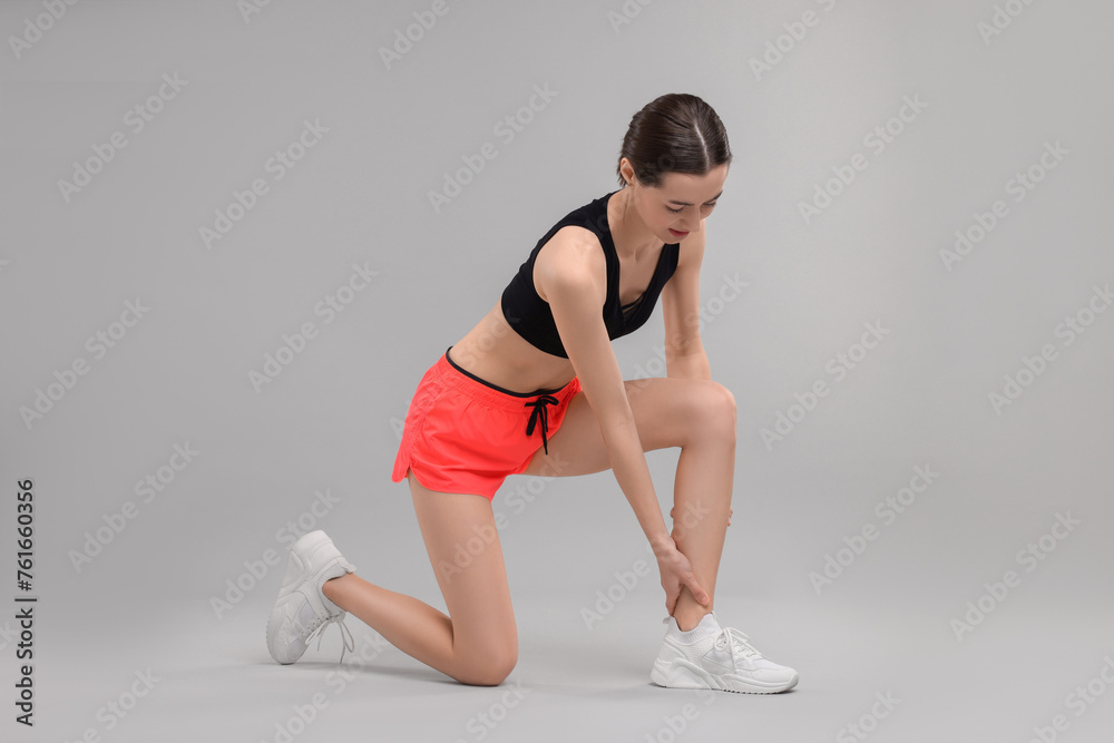 Young woman suffering from leg pain on grey background Young woman suffering from leg pain on grey background