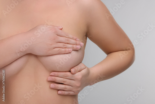 Mammology. Naked woman doing breast self-examination on light grey background  closeup
