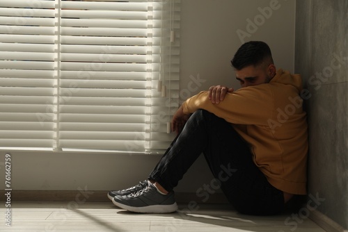 Sad man sitting on floor near window. Space for text