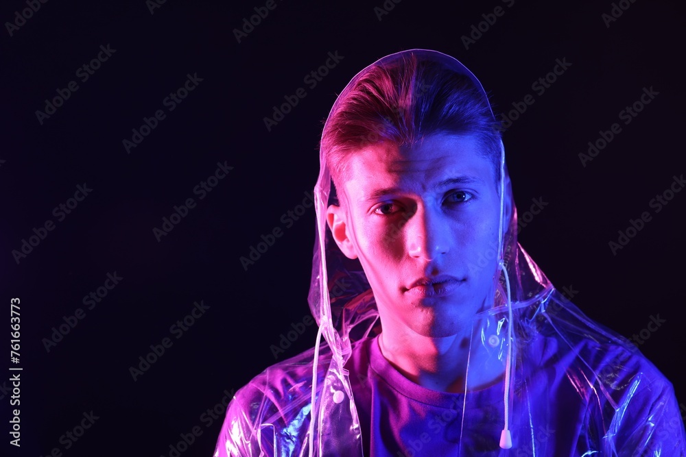 Young man wearing clear coat on dark background in neon lights. Space for text Young man wearing clear coat on dark background in neon lights. Space for text