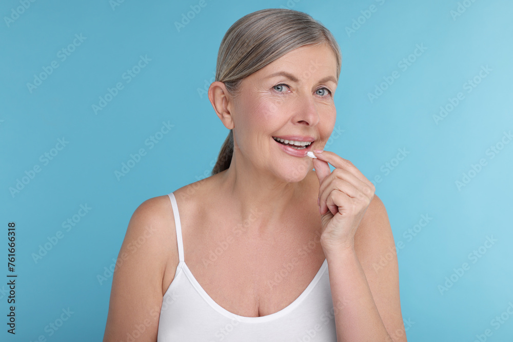 Beautiful woman taking vitamin pill on light blue background Beautiful woman taking vitamin pill on light blue background