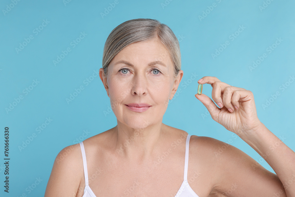 Beautiful woman with vitamin capsule on light blue background Beautiful woman with vitamin capsule on light blue background