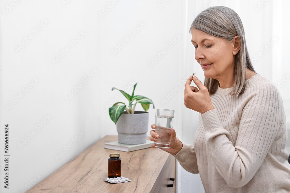 Beautiful woman taking vitamin pill at table indoors. Space for text Beautiful woman taking vitamin pill at table indoors. Space for text