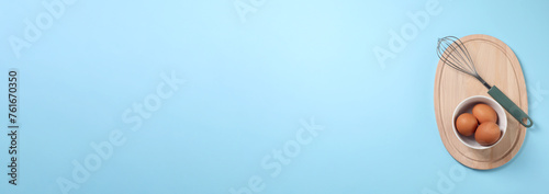 Whisk and eggs on light blue background, top view. Banner design with space for text