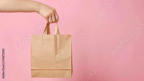 Male hand holding in hand brown clear empty blank craft paper bag for takeaway isolated on pastel pink background