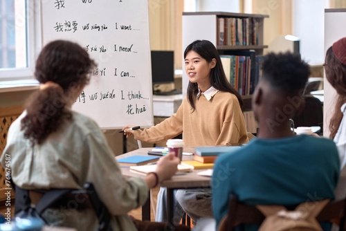 Portrait of smiling Asian female teacher explaining Chinese language grammar to students in library copy space photo