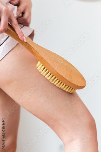 Using her fingers and thumb, a woman is brushing her thigh with a wooden brush. The fashion accessory brushes against her peachy skin, caressing her leg with care