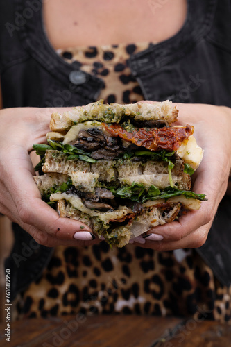 Dining in the restaurant. Closeup view of a woman holding a sliced multilayer vegetarian sandwich with fresh arugula  sun dried tomatoes  brie cheese and mushrooms.  