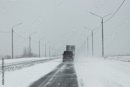 A car is traveling on a snowy highway, with the vehicles tires gripping the asphalt as it navigates the icy road surface under a grey sky