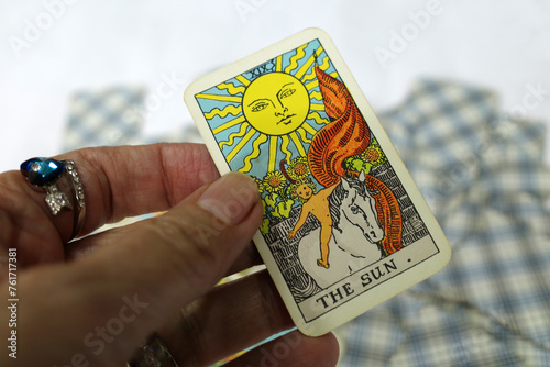 Hand of a fortune teller holding a tarot card in her hand. It's the sun. This card is generally considered positive. It stands for happiness and contentment, vitality, self-confidence and success