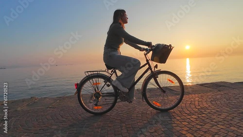 Young woman cycling along the shoreline in a city at sunset