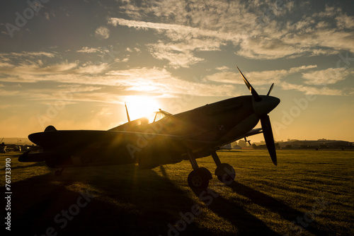The sun rises behind a Spitfire at an airshow and shines through the cockpit glass.