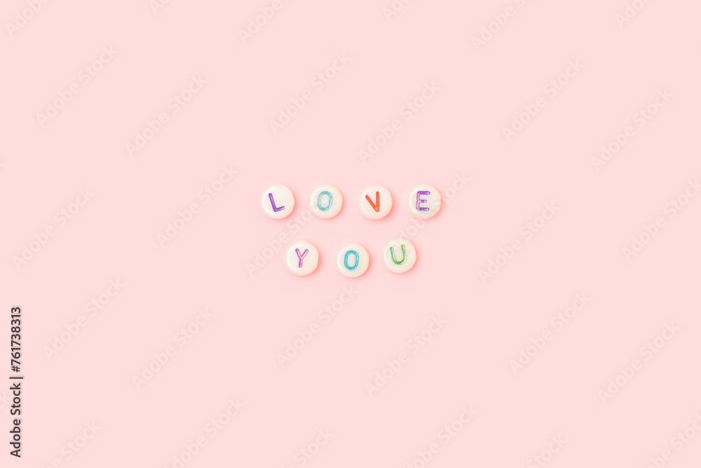Love you. Quote made of white round beads with colorful letters on a pink background. Valentines Day concept. Love you. Quote made of white round beads with colorful letters on a pink background. Valentines Day concept.