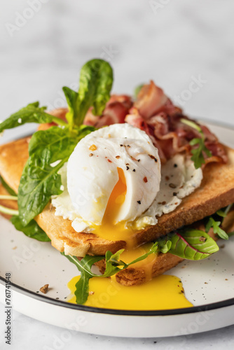 Toasts sandwich with poached egg, arugula, bacon and cream cheese on white plate marble background