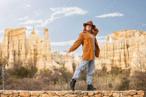 A woman in a brown jacket and hat poses in front of a mountain range photo