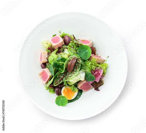 Healthy salad with seared tuna fish, lettuce, eggs, olives, onions and sauce in plate isolated on white background. Healthy food, top view