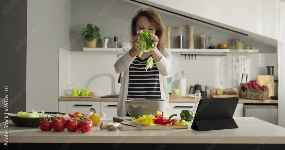 Cheerful woman prepares healthy salad at home, using cookbook app on digital tablet, fills a bowl with iceberg lettuce and romano. Homemade food. Healthy proper nutrition lifestyle Cheerful woman prepares healthy salad at home, using cookbook app on digital tablet, fills a bowl with iceberg lettuce and romano. Homemade food. Healthy proper nutrition lifestyle