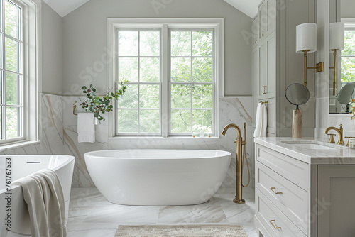 Elegant modern bathroom with white marble tiles  featuring a freestanding bathtub and golden fixtures by a large window.