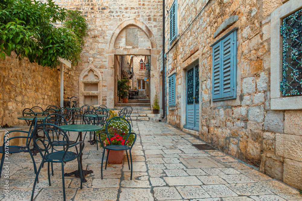 Cafe tables and chairs outside in old cozy street in the in old medieval town Hvar in outdoor restaurant with nobody, Dalmatia, Croatia. Popular travel and tourist destination on summer vacations