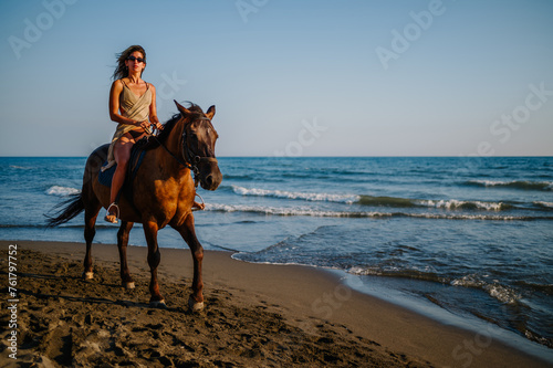 A seductive young lady is riding a horse on a beach near the sea.