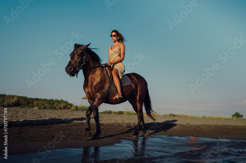 A charming young lady is horseback riding on a beach at sunset.