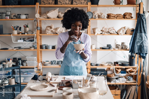 Interracial craftswoman at pottery workshop decorating clay work.