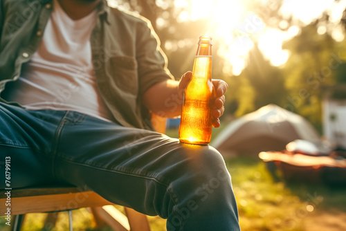 A young man sits alone on a summer street, holding a bottle of beer in his hand. Concept of sadness and loneliness with the unhealthy habit of alcohol consumption. photo