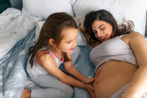 A picture of a pregnant mom smiling while her daughter rubs lotion on her belly or caressing the belly , spending quality time until the baby arrives © DusanJelicic