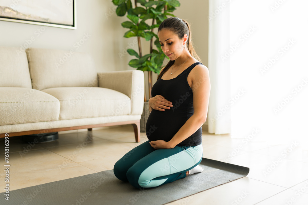 Relaxed expecting mother smiling touching her pregnant belly after exercising