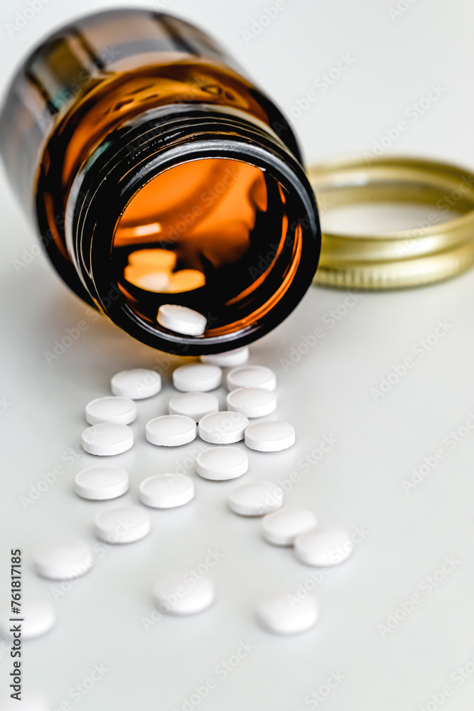 White Tablets Scattered on Table Next to Brown Glass Vial, on White Background, Close-up, Vertical Frame White Tablets Scattered on Table Next to Brown Glass Vial, on White Background, Close-up, Vertical Frame