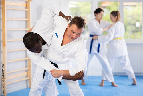 Multinational athletes in white kimonos practice Brazilian jiu Jitsu Aikido Wing chun wrestling. Training at Academy of Martial Arts martial arts hand-to-hand combat.